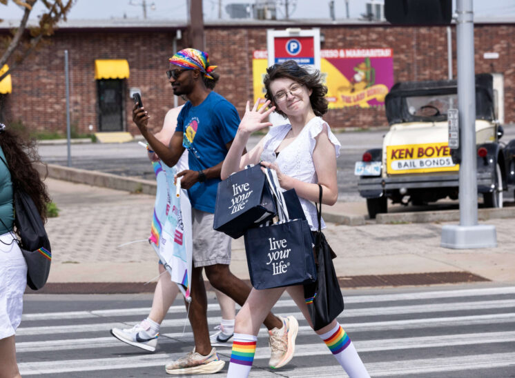 Parade attendees cross a downtown street while one person waves toward the camera.