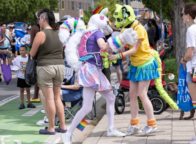 Two attendees in colorful animal-inspired costumes interact near the Pride parade route.