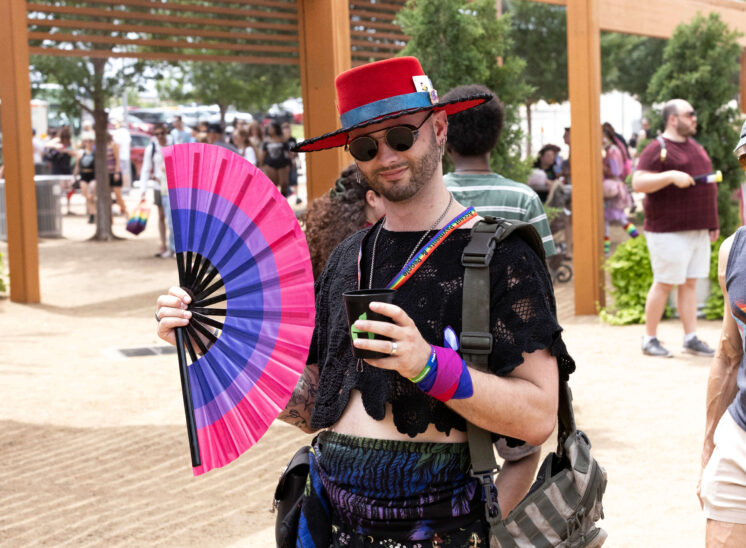 An attendee wearing a red hat and holding a colorful fan poses during the Pride festival.