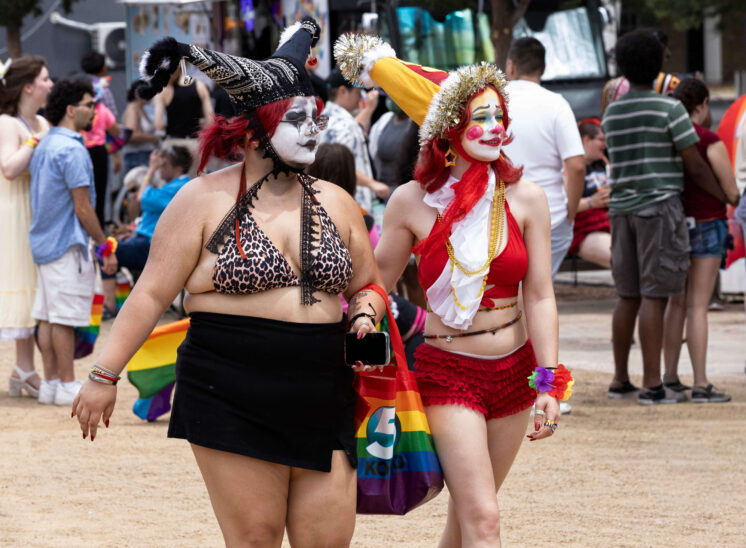 Two parade attendees in colorful clown-inspired costumes walk through the Oklahoma City Pride celebration.