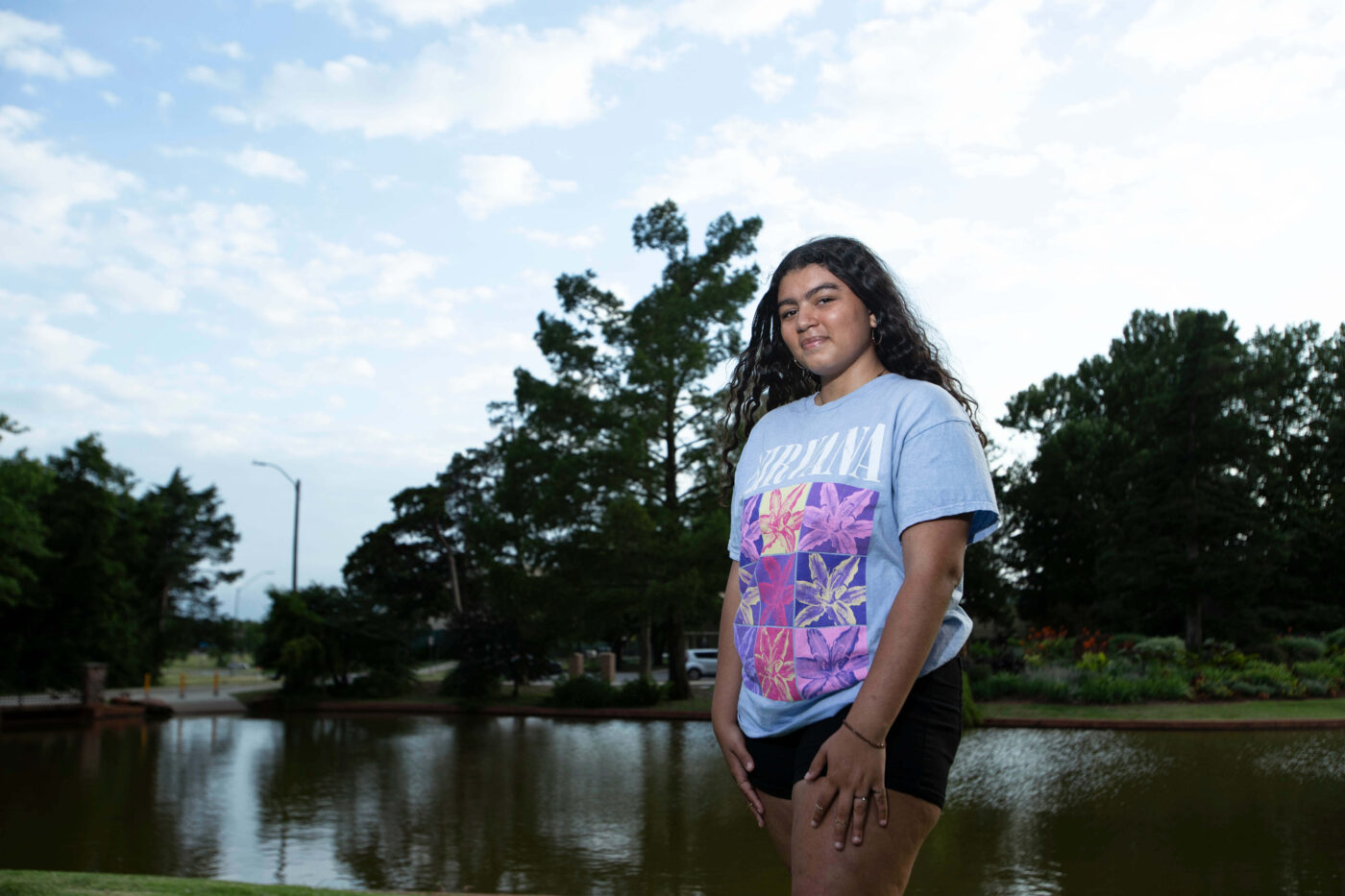 Close-up portrait of a young woman outdoors with blue sky and clouds in the background.