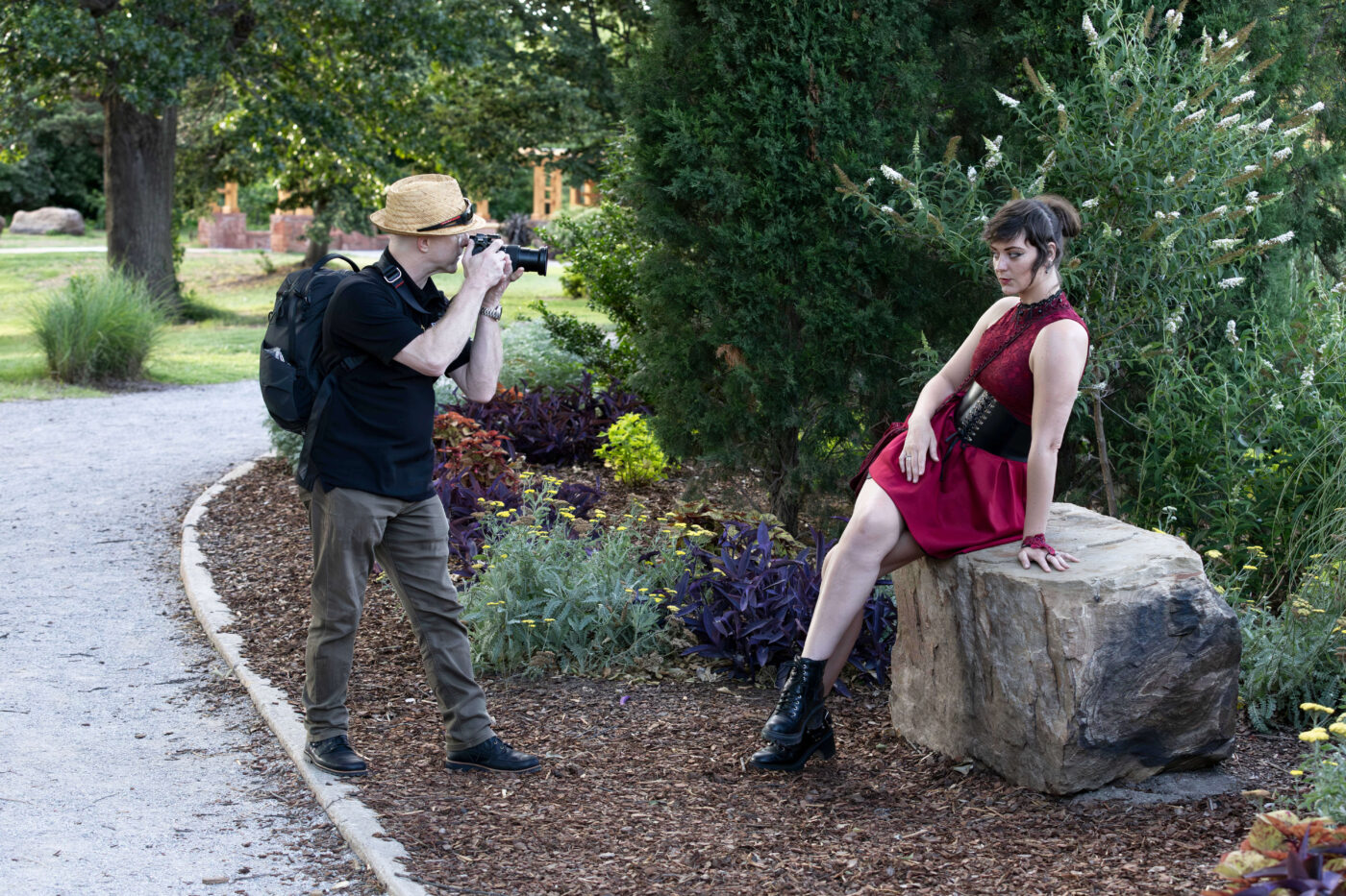 Photographer taking pictures of a model seated on a large stone in a garden setting.