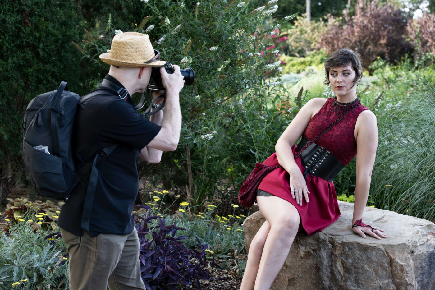 Photographer composing a portrait of a model seated on a stone surrounded by flowers and greenery.