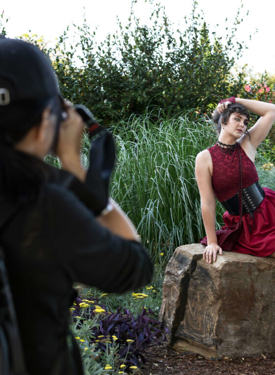 Photographer photographing a model seated on a stone while surrounded by ornamental grasses and flowers.