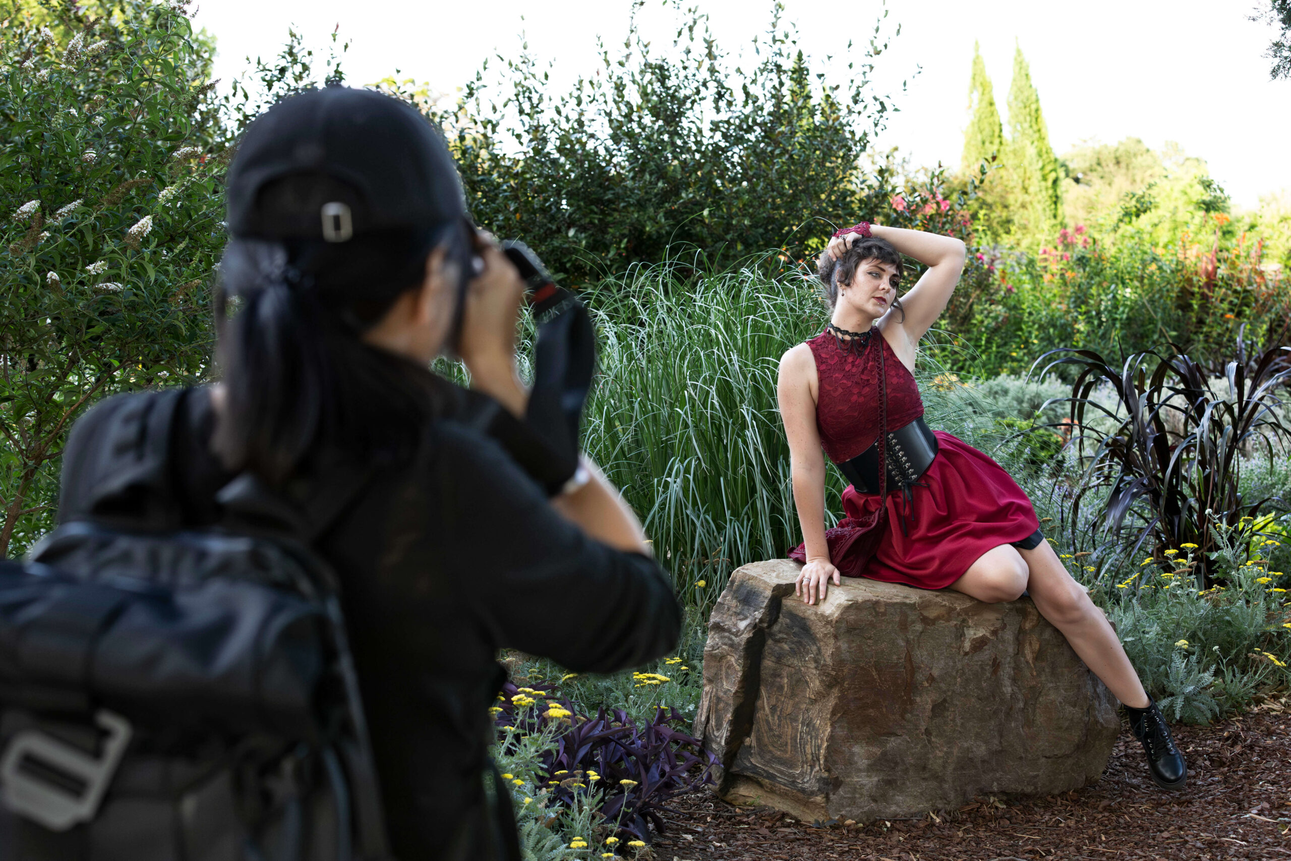 Photographer photographing a model seated on a stone while surrounded by ornamental grasses and flowers.