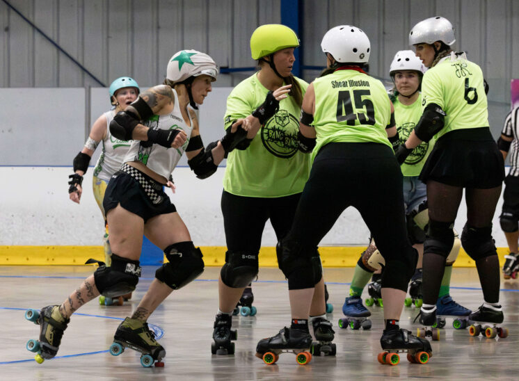 Capital City Crushers jammer attempts to break through a defensive wall formed by Twister City Roller Derby Outlaws skaters during a roller derby bout.