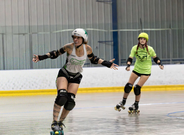 Capital City Crushers skater glides across the track with arms extended during a roller derby match against the Outlaws.