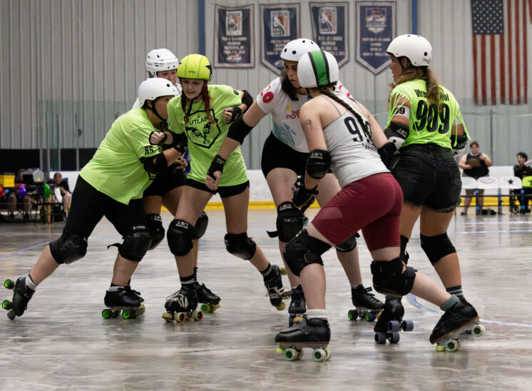 Twister City Roller Derby Outlaws blockers form a defensive wall against an approaching Capital City Crushers skater.