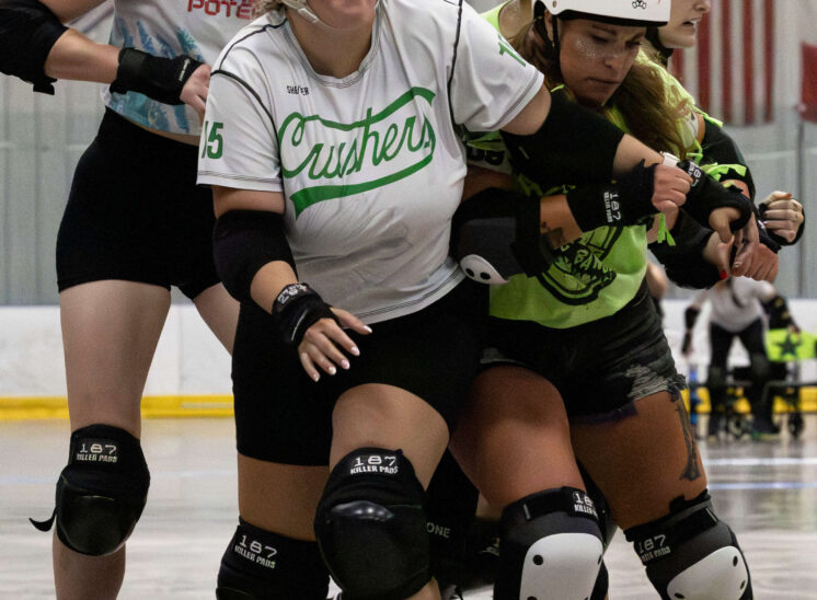 Capital City Crushers and Outlaws skaters engage in close contact while battling for position during a roller derby match.
