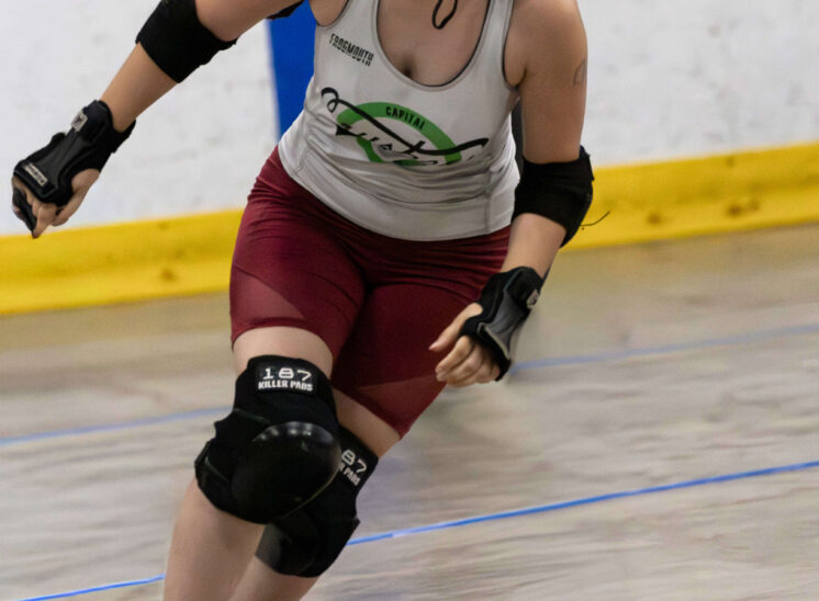 Capital City Crushers skater pushes through traffic while Outlaws defenders attempt to close the lane during a roller derby match.