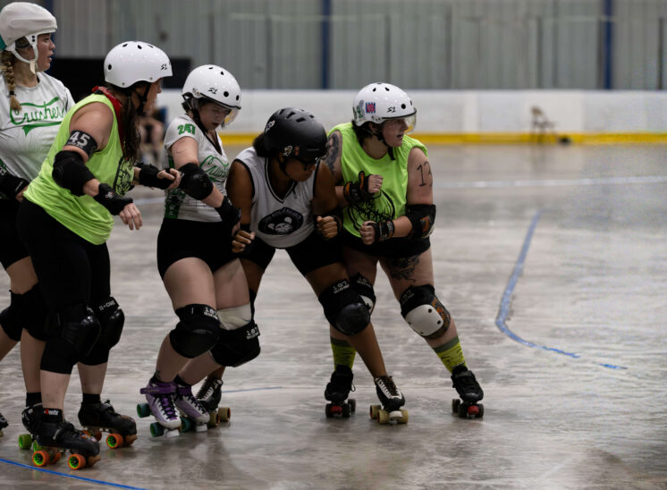 Roller derby skaters from the Outlaws and Crushers battle for track position near the inside line.