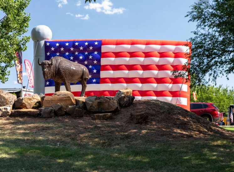 Buffalo statue standing on a rock display in front of a large inflatable American flag during Yukon Freedom Fest.