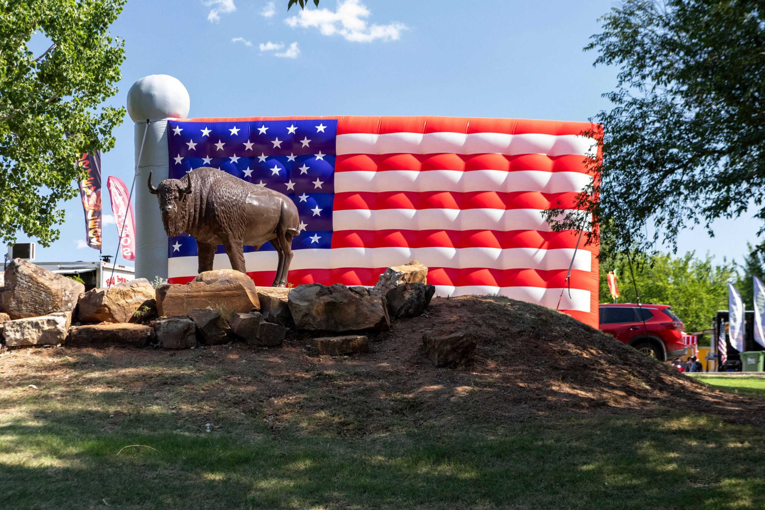 Buffalo statue standing on a rock display in front of a large inflatable American flag during Yukon Freedom Fest.