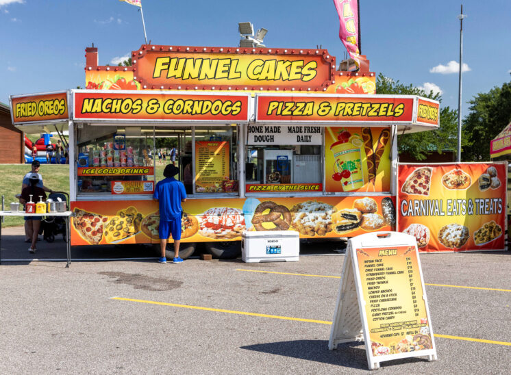 Concession stand selling funnel cakes, corn dogs, pizza, and other carnival foods.