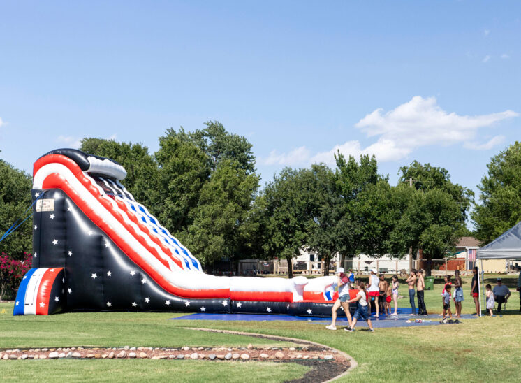 Large red, white, and blue inflatable water slide with families gathered nearby.