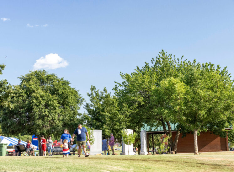 Families walking through the festival grounds beneath trees at Chisholm Trail Park.
