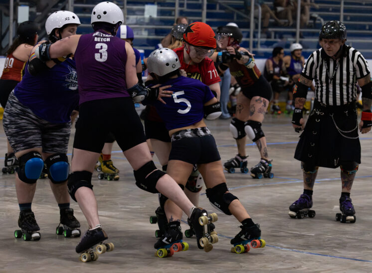 Twister City skater #5 pushes against Memphis B-Sides defenders during roller derby competition.