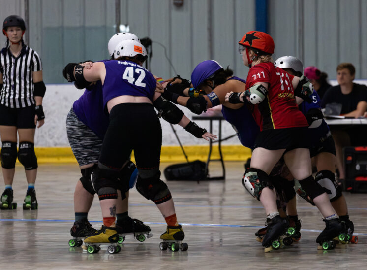 Twister City Lightning Quads and Memphis B-Sides blockers battle in a tightly packed roller derby formation.